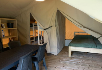 Interno di tenda safari al Camping Sonnenberg in Germania con tavolo da pranzo, letti a castello e letto matrimoniale.