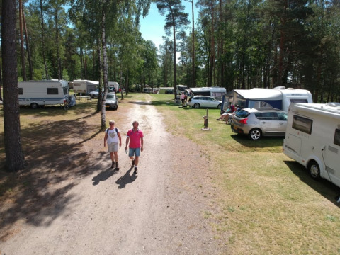 Due persone camminano su una strada sterrata tra roulotte e tende al Camping Sonnenberg in Germania.
