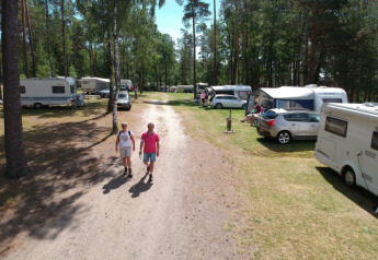 Due persone camminano su una strada sterrata tra roulotte e tende al Camping Sonnenberg in Germania.