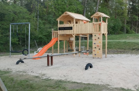 Spielplatz mit Holzhütten, Rutsche, Schaukeln und Kletterwand auf Camping Sonnenberg in Deutschland.
