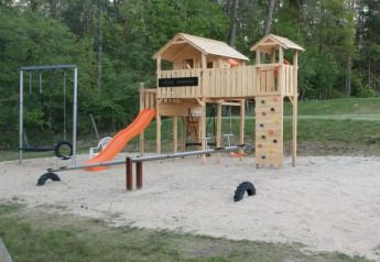 Parco giochi con casette in legno, scivolo, altalene e parete da arrampicata al Camping Sonnenberg, Germania.