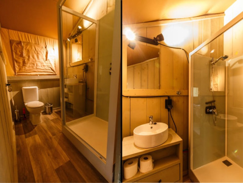 Baño dentro de una tienda safari con ducha, inodoro y lavabo, decorado y con iluminación cálida.
