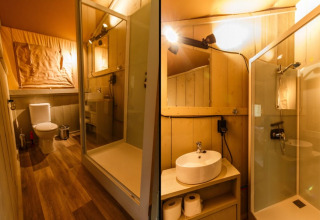 Interior of a safari tent bathroom with shower, toilet, and sink, warmly lit and neatly arranged.