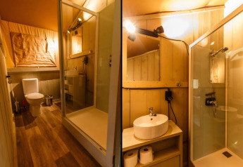 Interior of a safari tent bathroom with shower, toilet, and sink, warmly lit and neatly arranged.
