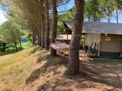 Tienda safari con baño privado bajo pinos, hamaca y vistas al lago y bosque de fondo.