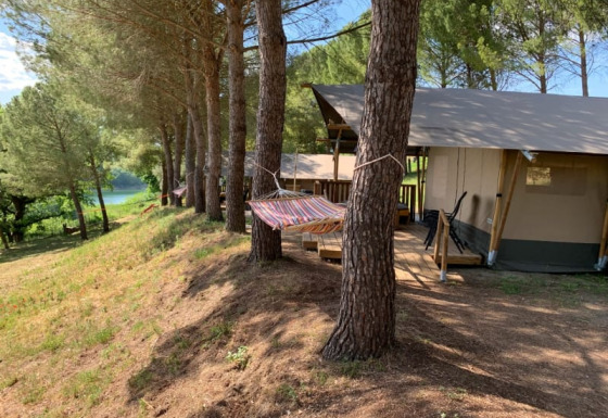 Tienda safari con baño privado bajo pinos, hamaca y vistas al lago y bosque de fondo.