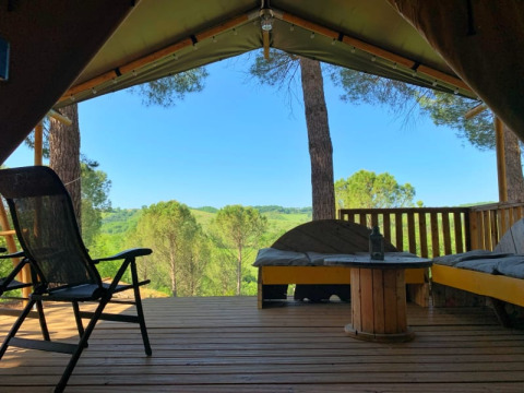 Udsigt fra en safaritelts terrasse med sofaer og stole, omgivet af træer og bakker i Italien.