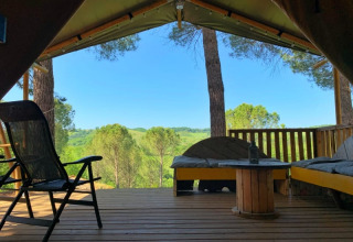 Udsigt fra en safaritelts terrasse med sofaer og stole, omgivet af træer og bakker i Italien.