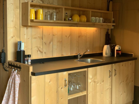 Knus houten keukentje in een safaritent met zwart aanrechtblad, spoelbak en open planken met servies.