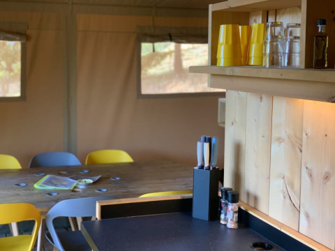 Cocina y comedor en una tienda safari con mesa de madera, vasos amarillos y cuchillos en Casa & Glamping Sorriso.