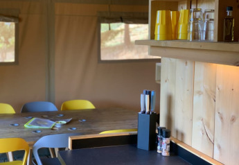 Cocina y comedor en una tienda safari con mesa de madera, vasos amarillos y cuchillos en Casa & Glamping Sorriso.