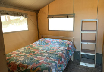 Interior de la tienda Safari tent + sanitair en Casa & Glamping Sorriso, Italia, con cama y estantería.