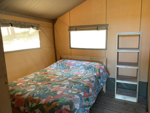 Interno della Safari tent + sanitair a Casa & Glamping Sorriso in Italia con letto matrimoniale e scaffale.
