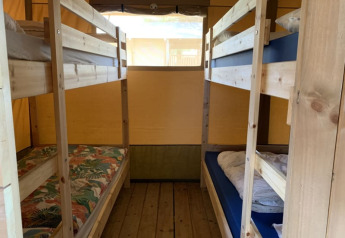 Interior of a safari tent with wooden bunk beds and floor at Casa & Glamping Sorriso in Italy.