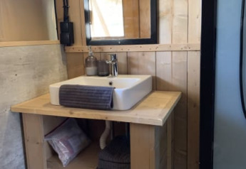 Baño de una tienda safari con mueble de madera, espejo y estantes en Casa & Glamping Sorriso, Italia.
