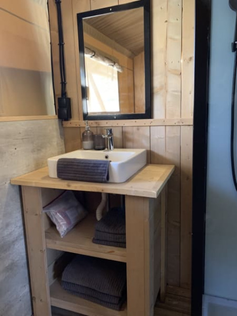 Baño de una tienda safari con mueble de madera, espejo y estantes en Casa & Glamping Sorriso, Italia.