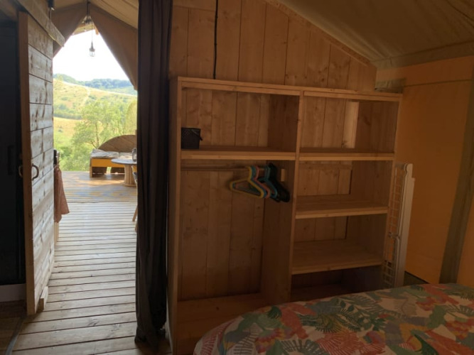 Intérieur d'une tente safari à Casa & Glamping Sorriso, étagères en bois, terrasse et vue sur la nature.