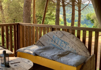 Terraza de madera con banco y vista al bosque en Safari tent + sanitair, Casa & Glamping Sorriso, Italia.