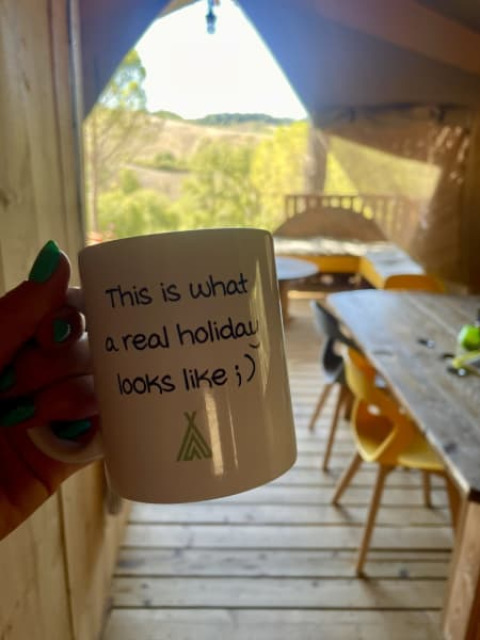 Hand houdt beker met tekst in safaritent met houten veranda bij Casa & Glamping Sorriso, Italië.