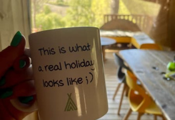 Hand houdt beker met tekst in safaritent met houten veranda bij Casa & Glamping Sorriso, Italië.