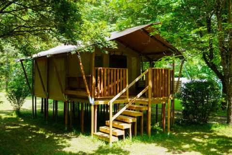 Tenda safari presso Camping Pittoresque in Francia, rialzata su palafitte e immersa nel verde boschivo.