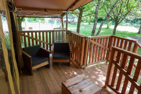 Holzterrasse mit Stühlen an einem Safarizelt auf Camping Pittoresque, umgeben von Bäumen in Frankreich.