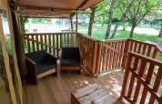 Terraza de madera con sillones junto a tienda safari en Camping Pittoresque, rodeada de árboles en Francia.