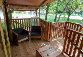 Terraza de madera con sillones junto a tienda safari en Camping Pittoresque, rodeada de árboles en Francia.