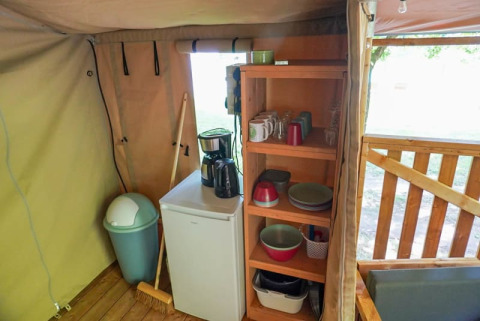 Vista interna di una tenda safari con angolo cottura, mini frigo, scaffali in legno e macchina da caffè.