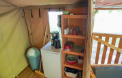 Vista interior de una tienda safari con una pequeña cocina, mini nevera, estantería y cafetera.