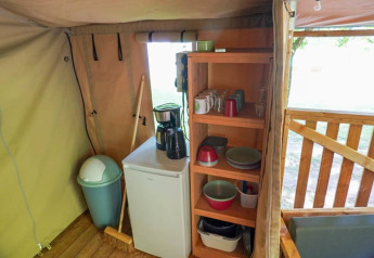 Binnenaanzicht van een safaritent met keukentje, mini-koelkast, houten rek en koffiezetapparaat.