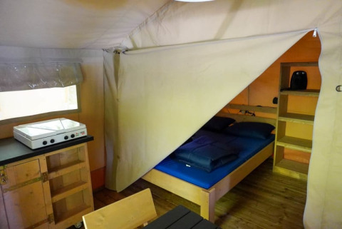 Vista interna di una tenda safari al Camping Pittoresque in Francia con letto, scaffali e fornello.