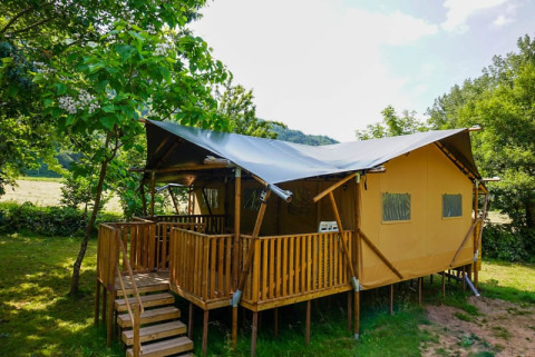 Safari-Zelt mit Holzterrasse im Grünen auf Camping Pittoresque, Frankreich, an einem sonnigen Tag.