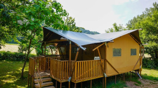 Safaritent met houten terras bij Camping Pittoresque in Frankrijk, omringd door groene bomen.