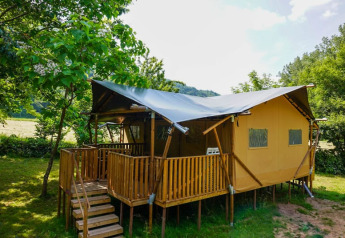Tienda safari con terraza de madera en Camping Pittoresque, Francia, rodeada de naturaleza verde.
