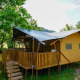 Tienda safari con terraza de madera en Camping Pittoresque, Francia, rodeada de naturaleza verde.