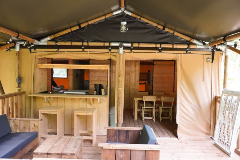 Innenansicht eines Safarizeltes mit Holzmöbeln und Sitzbereichen bei Camping Pittoresque in Frankreich.