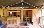 Vista interior de una tienda safari con muebles de madera y comedor en Camping Pittoresque, Francia.