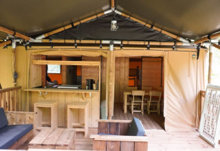 Vista interior de una tienda safari con muebles de madera y comedor en Camping Pittoresque, Francia.