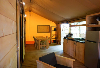Vista interior de una tienda safari con cocina, mesa de comedor y muebles de madera en Camping Pittoresque, Francia.