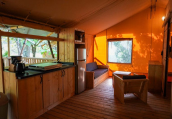 Interior de tienda safari con cocina y zona de estar en Camping Pittoresque en Francia, muebles de madera.