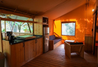 Safari tent interior with kitchen and seating at Camping Pittoresque, France, featuring wood furnishings.