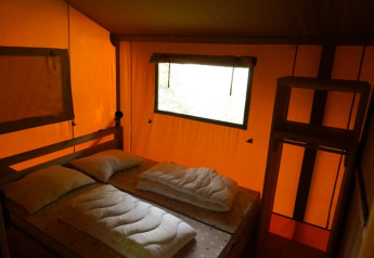 Vista interior de una tienda safari con cama doble y ventana en Camping Pittoresque, Francia.