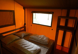 Vista interior de una tienda safari con cama doble y ventana en Camping Pittoresque, Francia.