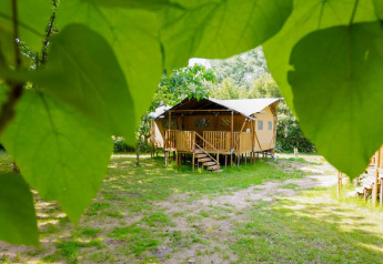 Tienda safari con baño privado en Camping Pittoresque, Francia, vista a través de hojas verdes.