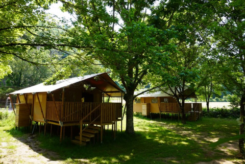 Safari-Zelt mit eigenem Sanitärbereich auf dem Campingplatz Pittoresque in Frankreich, umgeben von Bäumen.