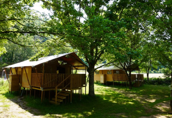 Safaritent met privé sanitair op Camping Pittoresque in Frankrijk, omringd door groene bomen.