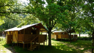 Tenda safari con servizi igienici privati al Camping Pittoresque in Francia, immersa tra alberi verdi.