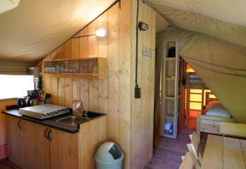 Interior de una tienda safari con cocina y literas en Camping Pittoresque, Francia.