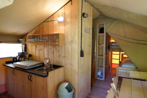 Interior de una tienda safari con cocina y literas en Camping Pittoresque, Francia.